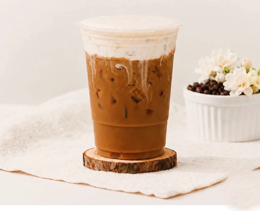 Iced Jasmine Cream Coffee with a cream top on a wooden coaster, jasmine flowers beside it